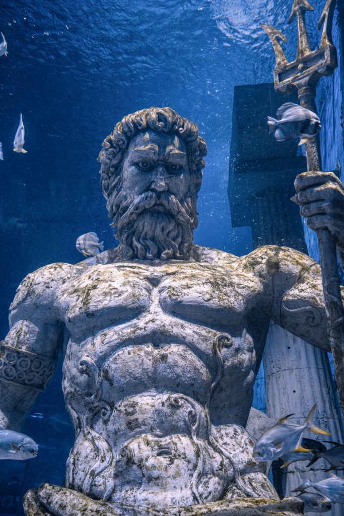 a stone statue in the water representing a bearded man with a trident