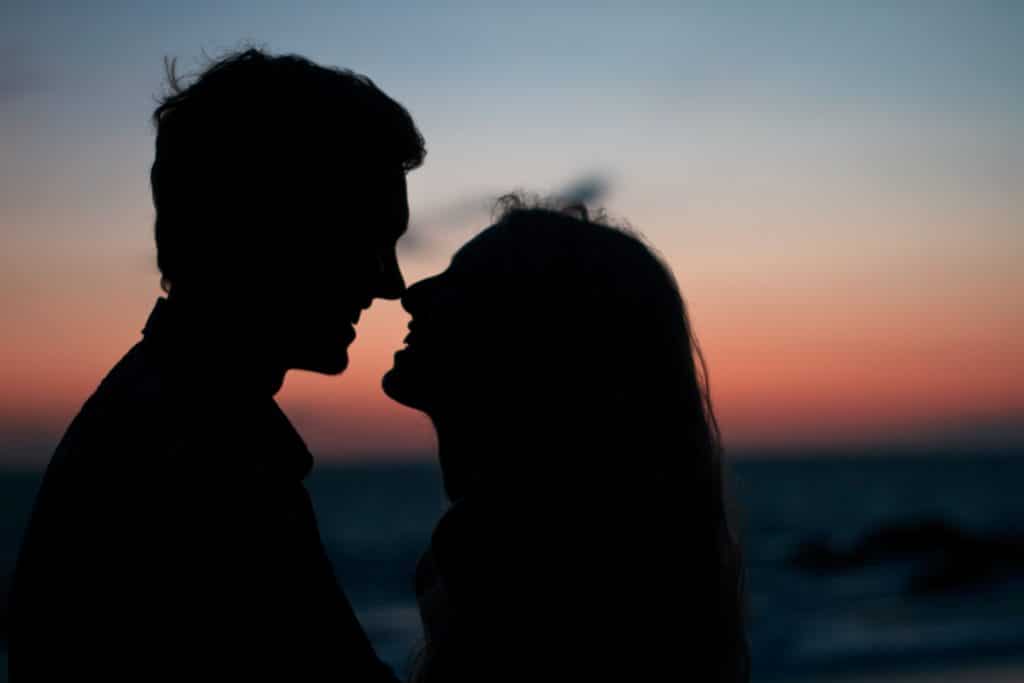 a woman and a man who are kissing in front of the sunset 