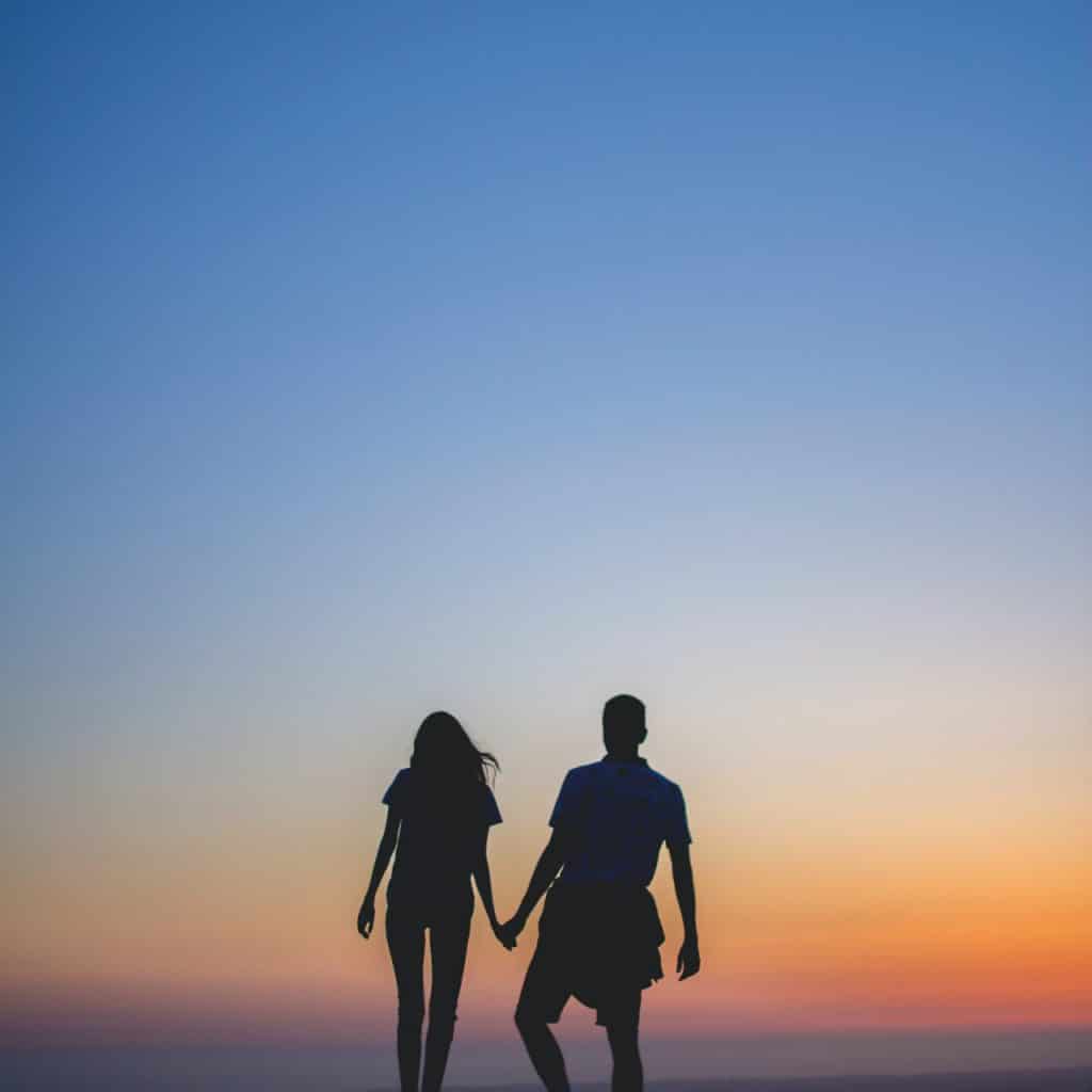a couple holding hands in front of the setting sun
