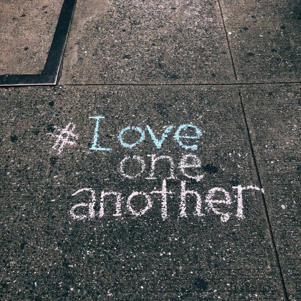 the phrase love one another written on the floor in chalk