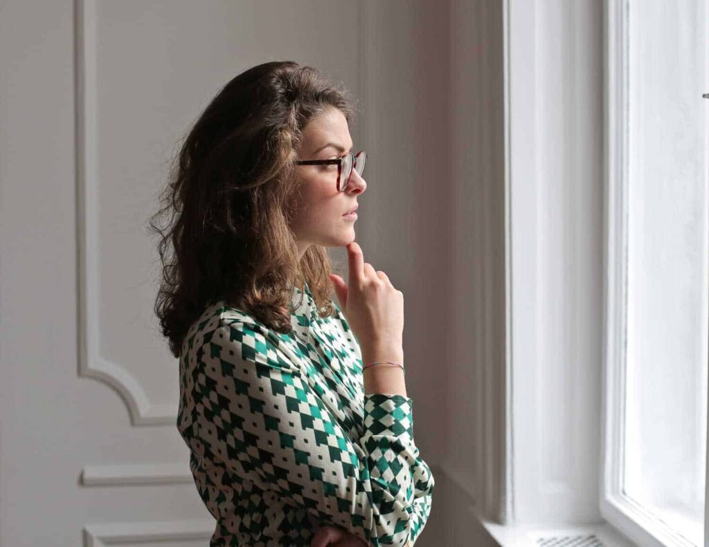 Young woman in spectacles keeping hand on chin and looking away