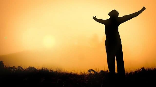 An optimistic man hugging the sun with his outstretched arms