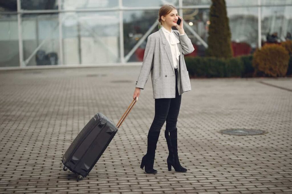 woman carrying baggage and talking on smartphone near airport