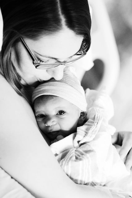 woman with glasses lovingly kisses her newborn baby