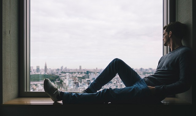 a man sitting on a window sill, gazing at a cityscape