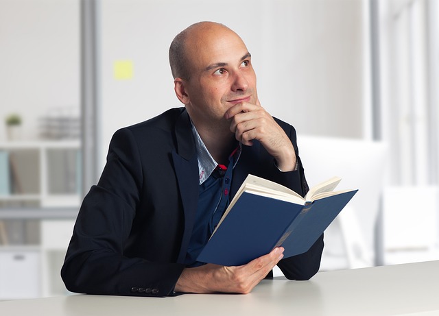 man in a suit reading a book at a desk