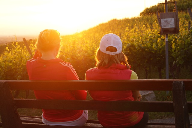 two women enjoying the sunset while sitting on a bench