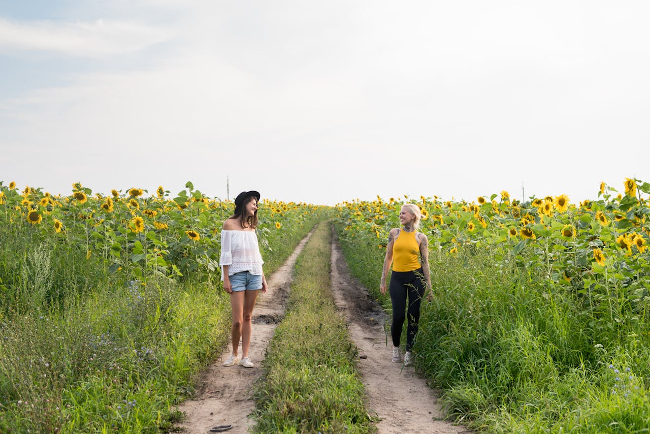two women walking through a sunflower field