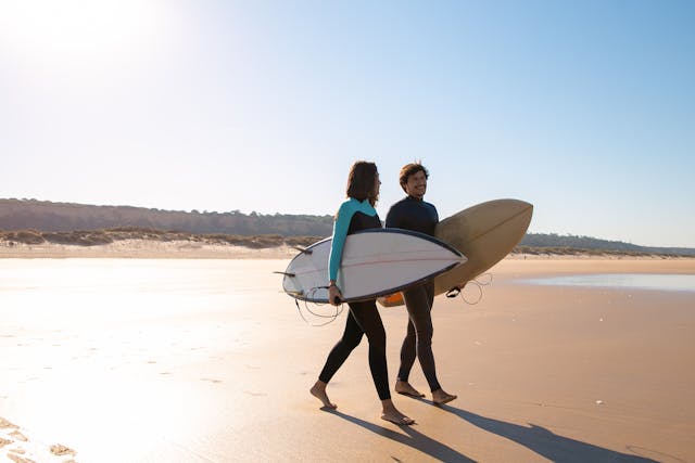 a couple carrying surfboards walks along the beach