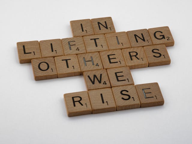 positive message spelled with scrabble tiles – in lifting others, we rise