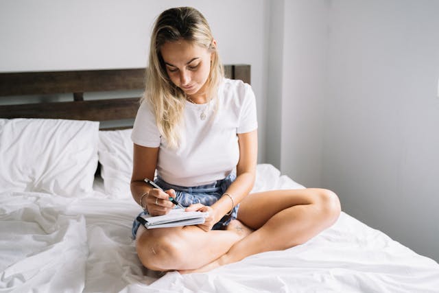 a woman taking notes of her dreams the night before while sitting on her bed