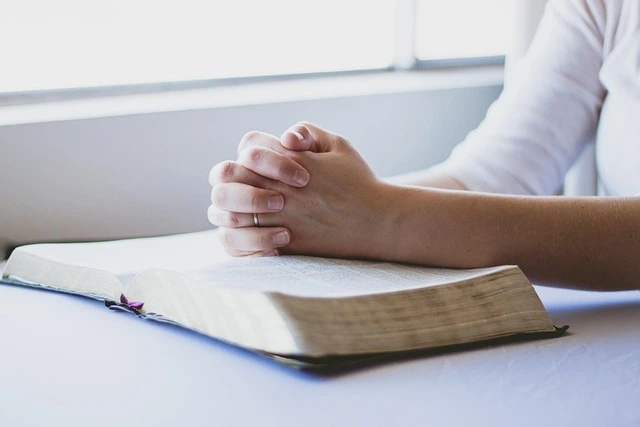 Close-up of clasped hands in prayer resting on an open Bible | Trusted Astrology