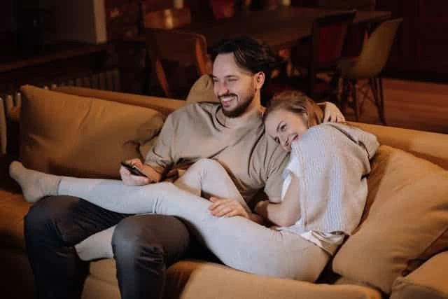 Smiling couple relaxing on a couch together while looking at a smartphone | Trusted Astrology