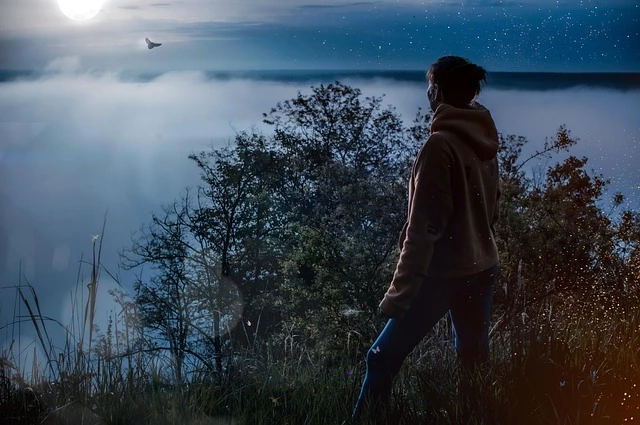 woman in a hoodie overlooking a misty, starry valley at night | Trusted Astrology